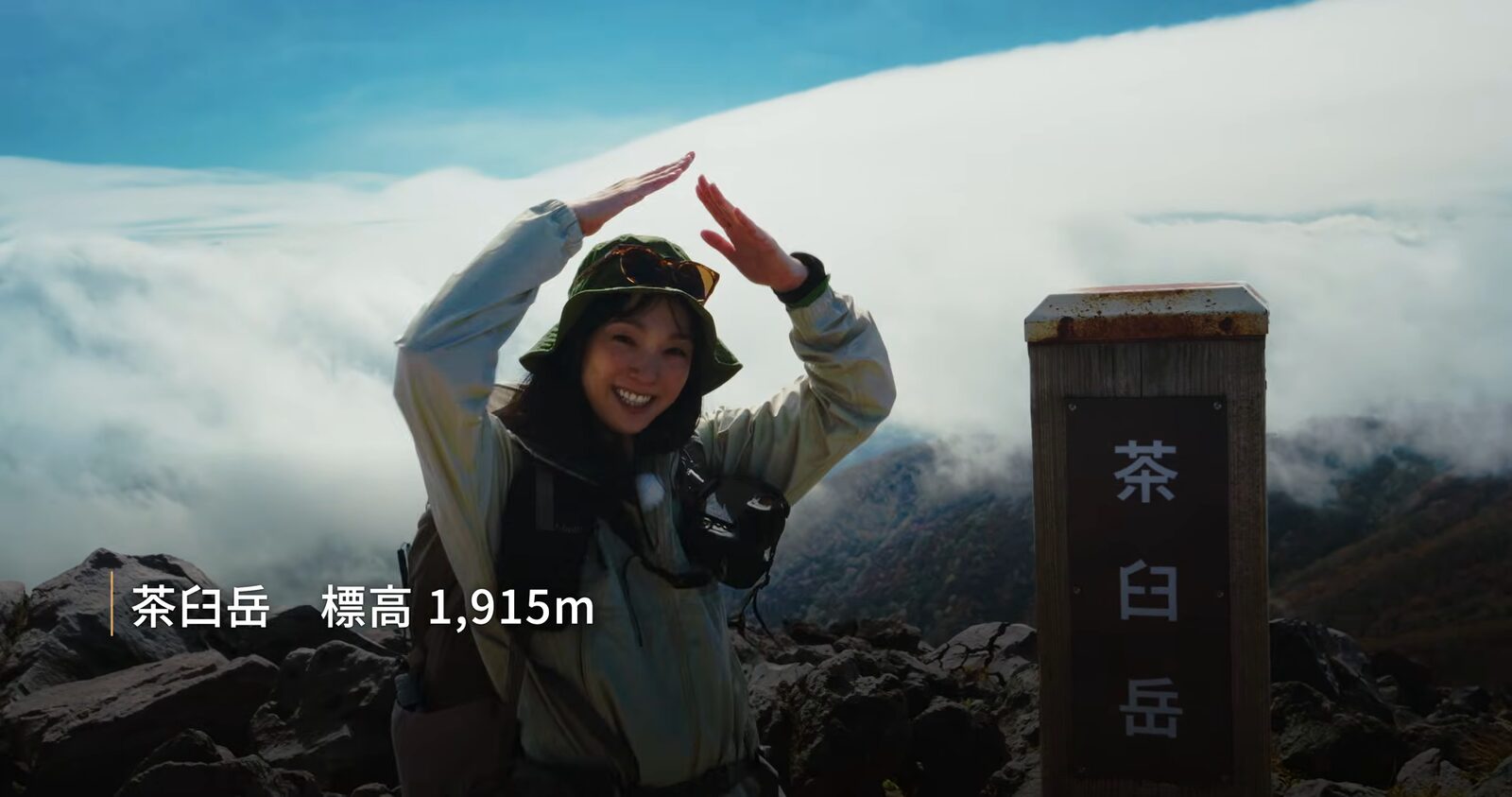 雲海を背に茶臼岳の山頂標識の横でポーズをとる岩崎良美